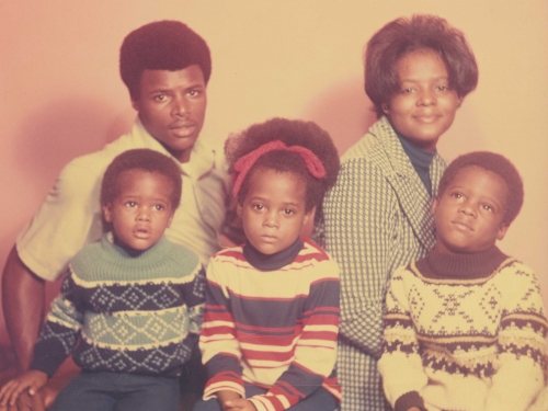 A man and woman sitting on the back of a bench with two little boys and a girl on the front.